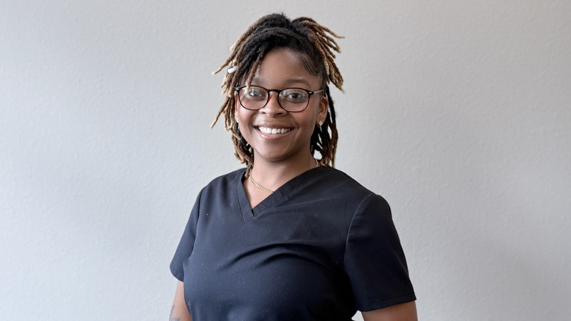 A person smiling while standing up against a blank wall
