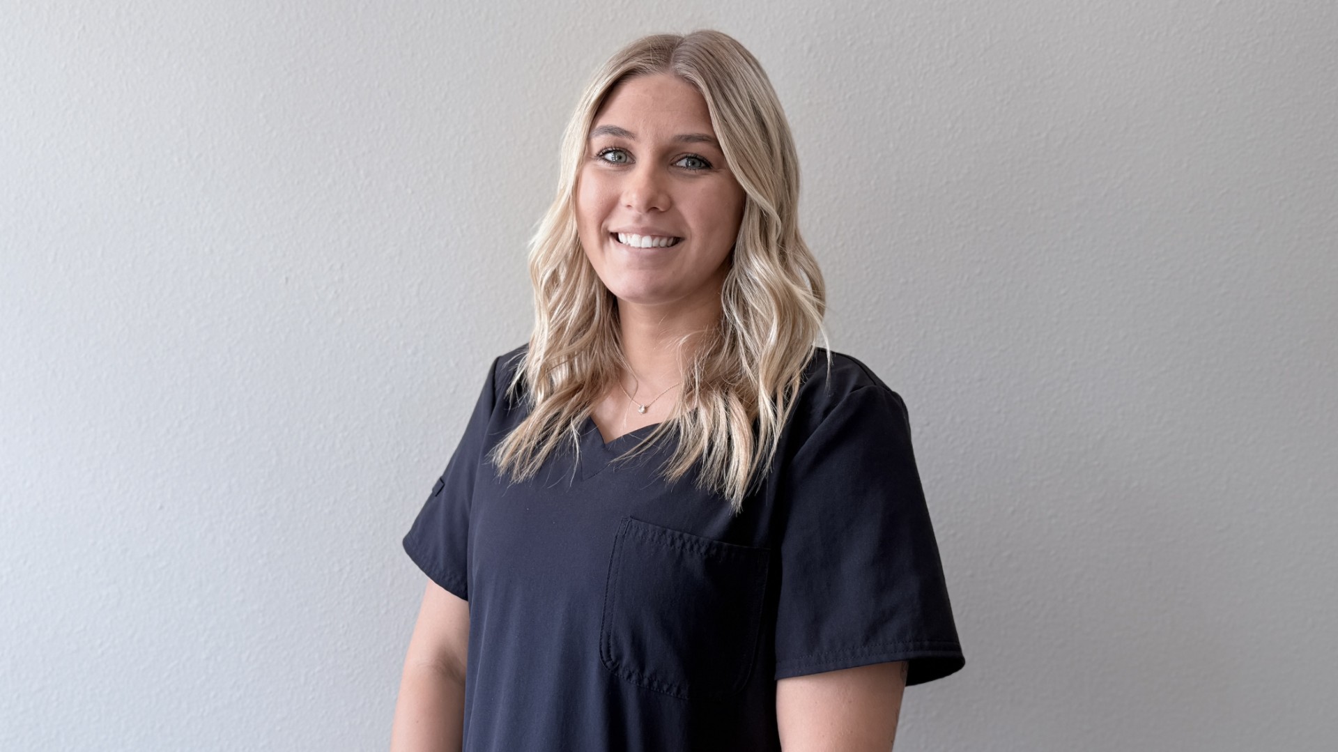 A person smiling while standing up against a blank wall