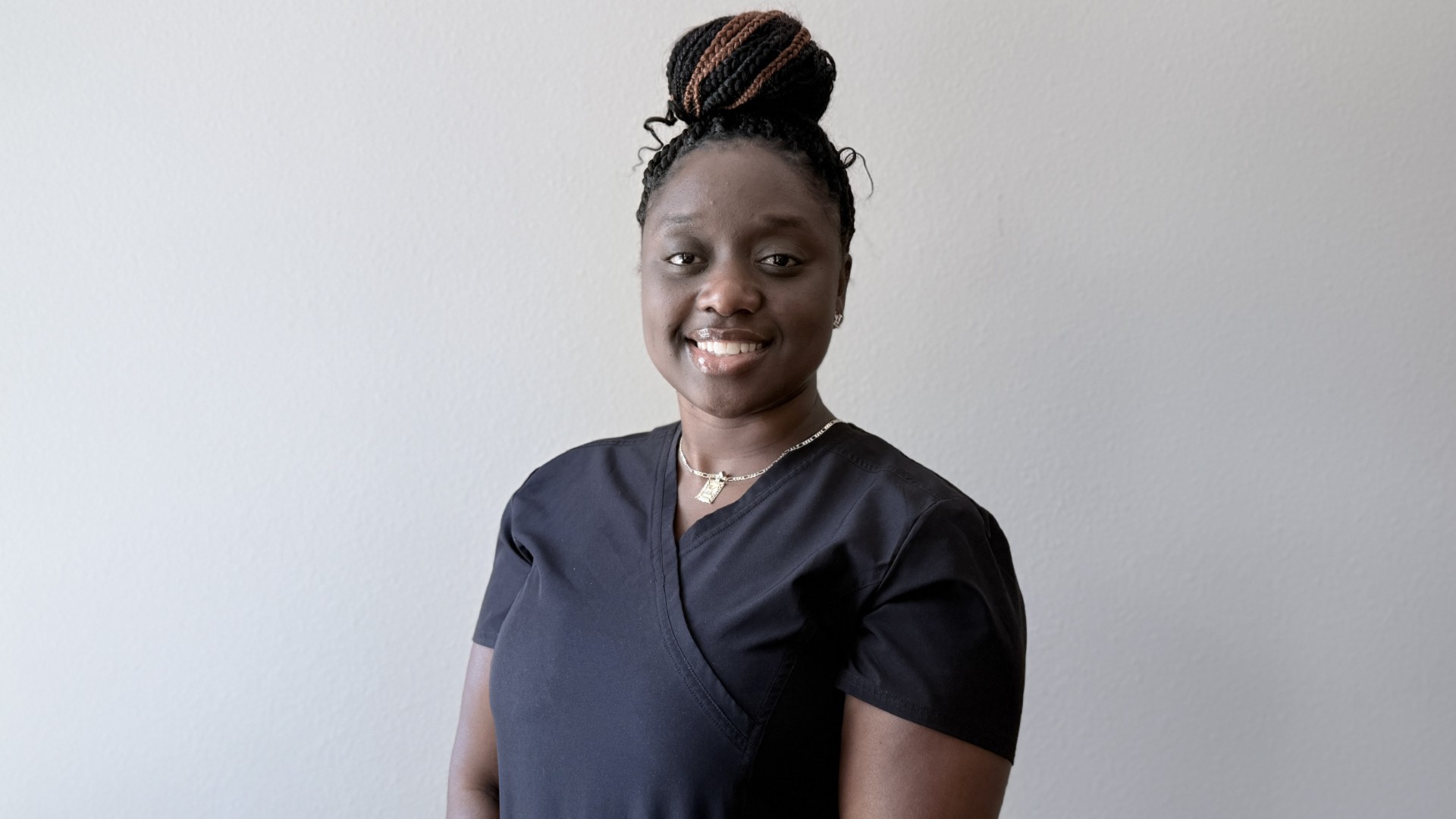 A person smiling while standing up against a blank wall