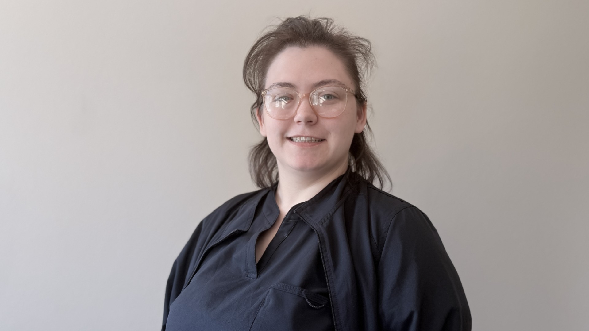 A person smiling while standing up against a blank wall