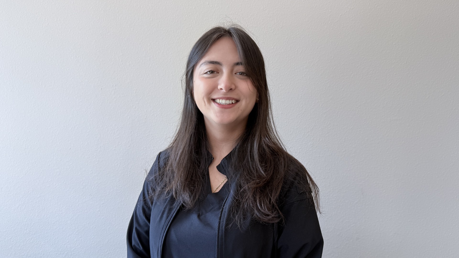 A person smiling while standing up against a blank wall