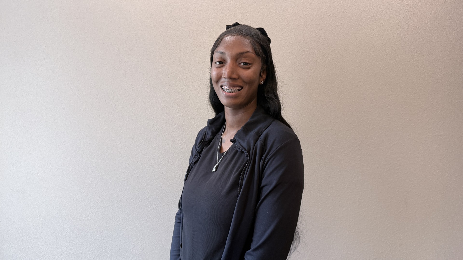 A person smiling while standing up against a blank wall